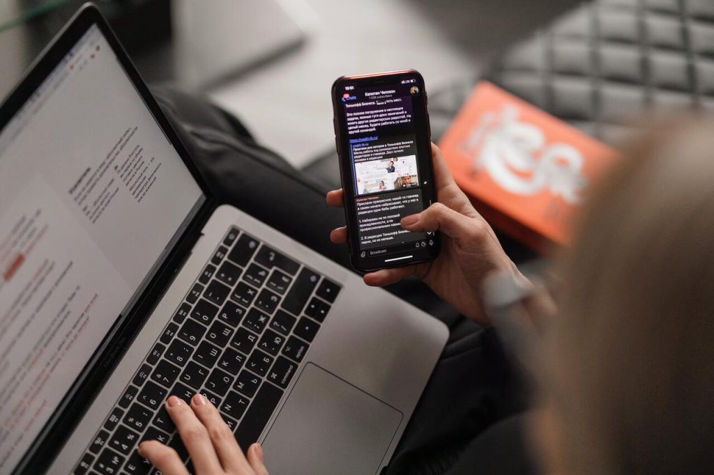 Mulher fazendo pesquisas em celular e em notebook, possivelmente buscando informações sobre cursos complementares de administração.